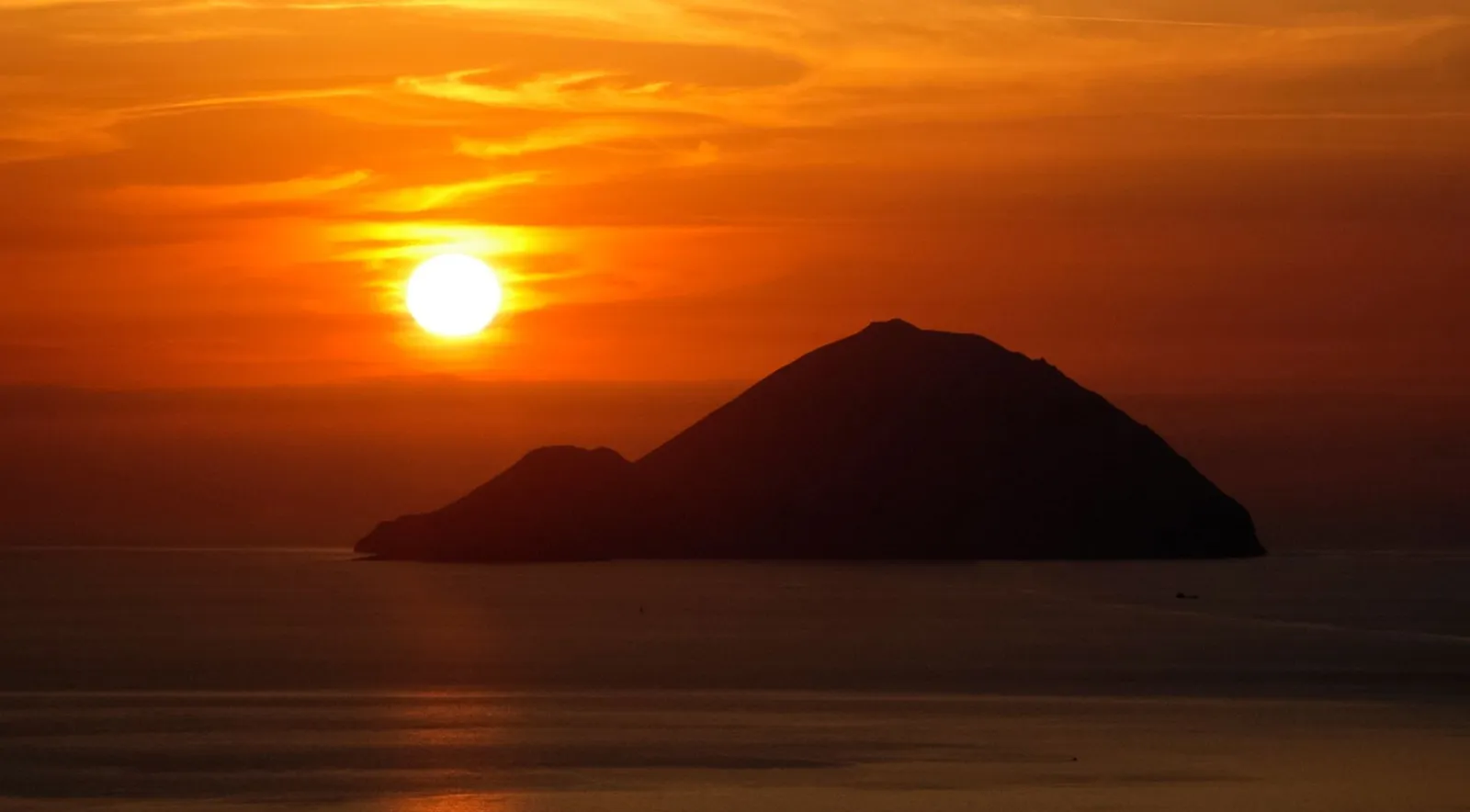 The sun setting behind the silhouette of an island