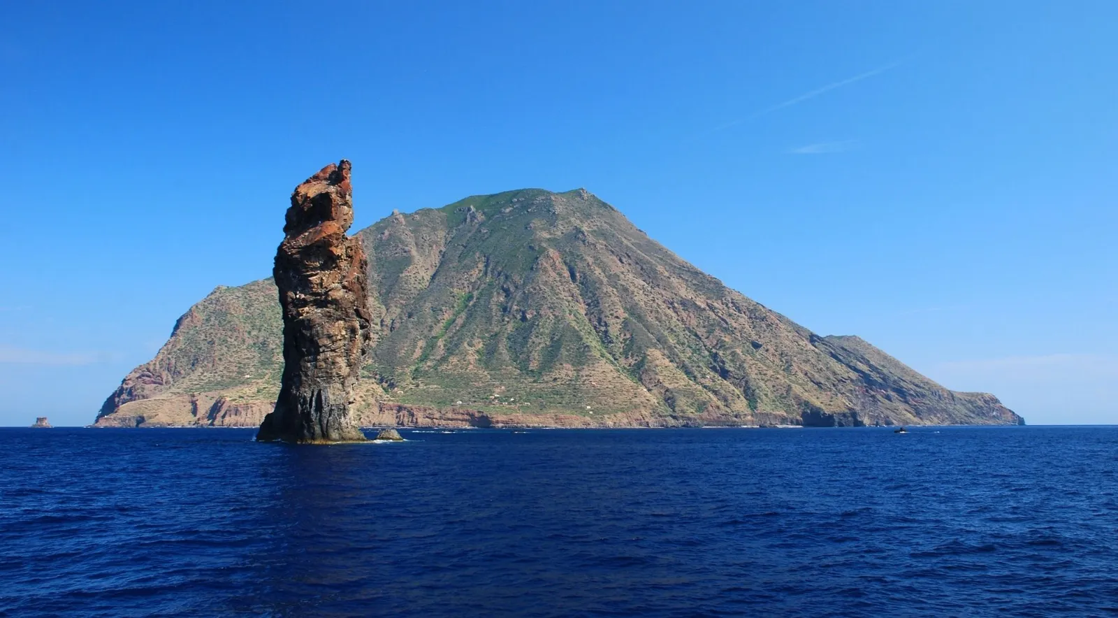 A tall sea stack in front of a green volcanic island