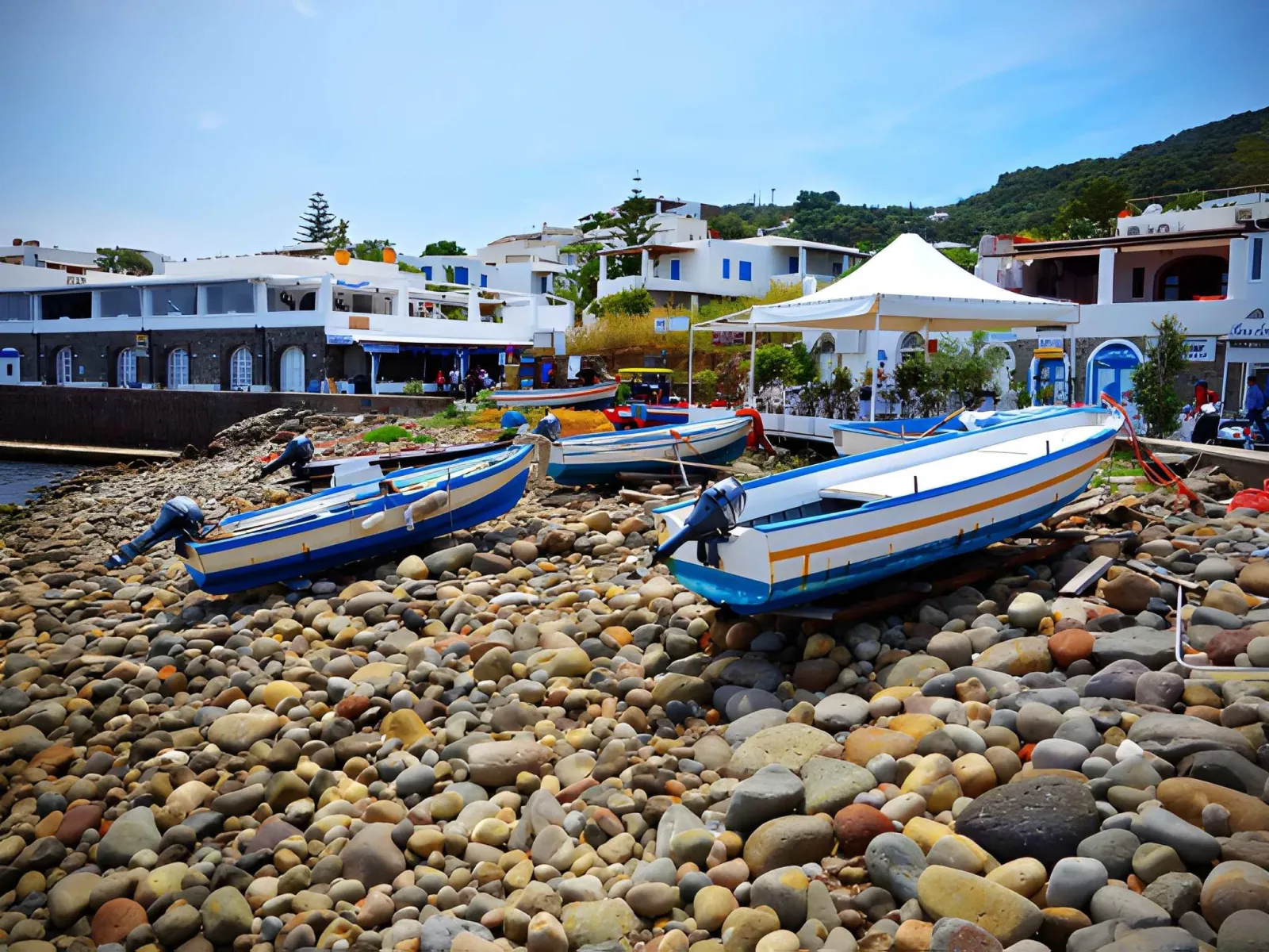 Small boats pulled up on a pebble beach below white houses