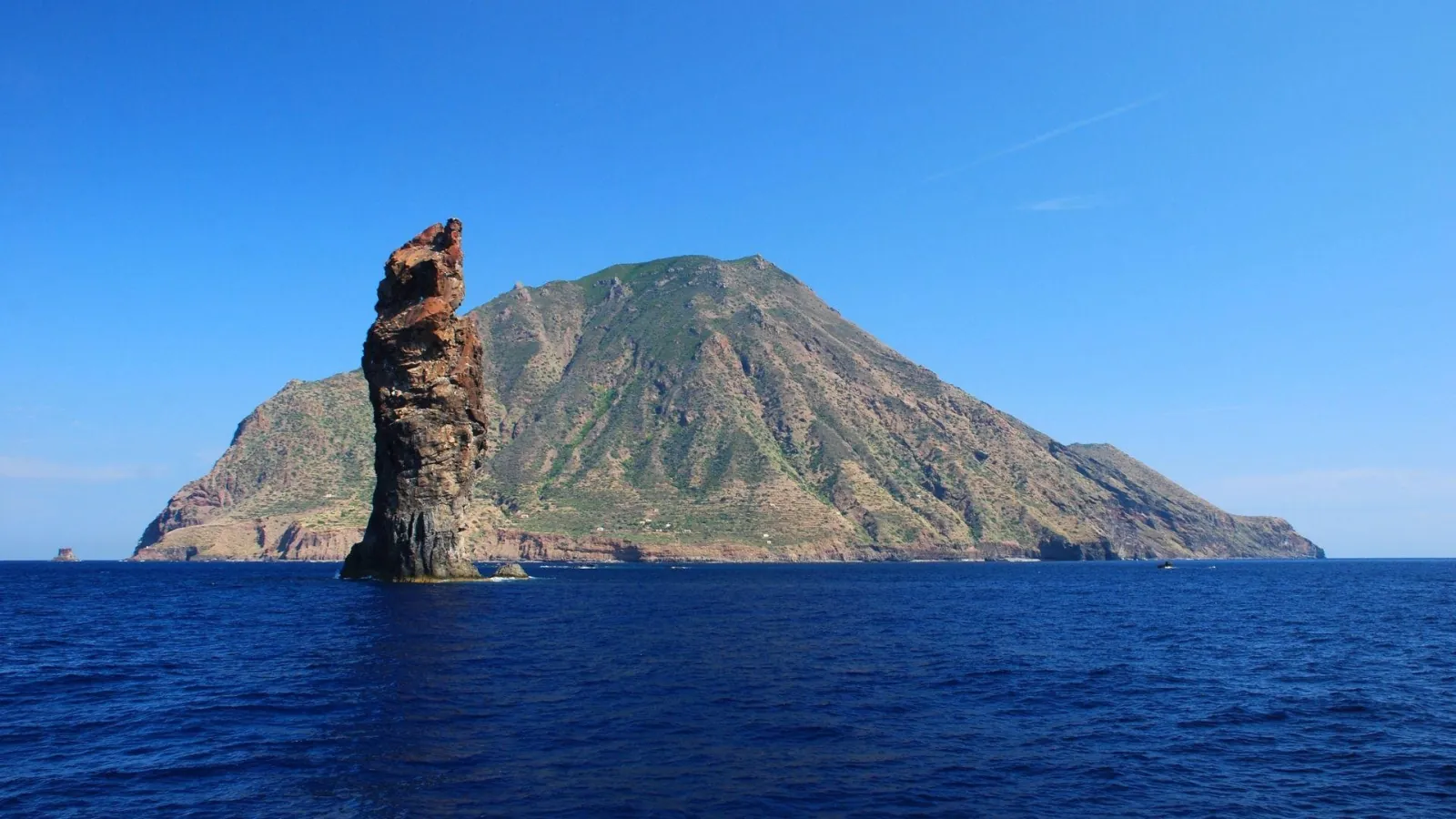 A sea stack in front of a green volcanic island