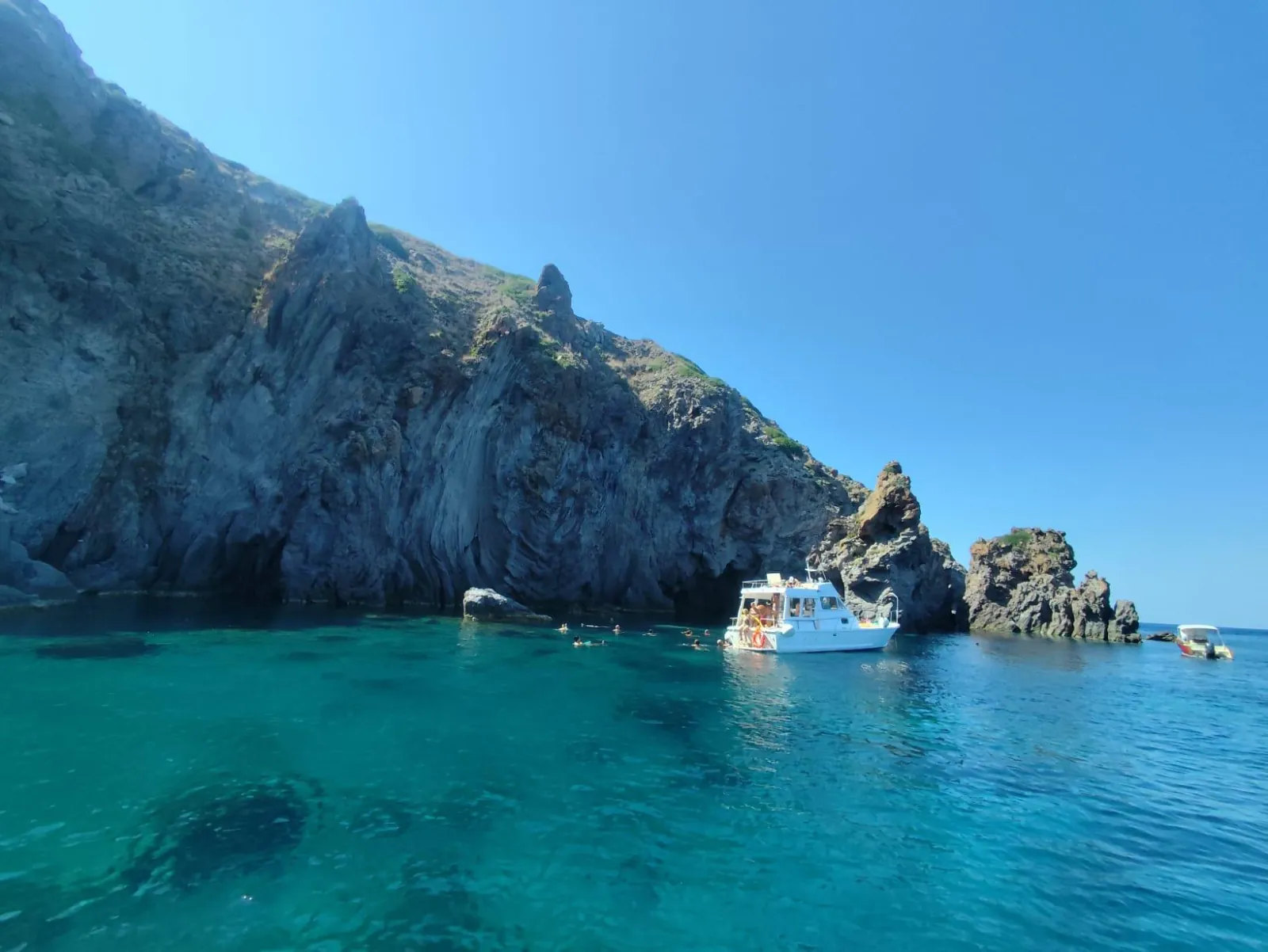 Small boat anchored below cliffs in turquoise water off Panarea