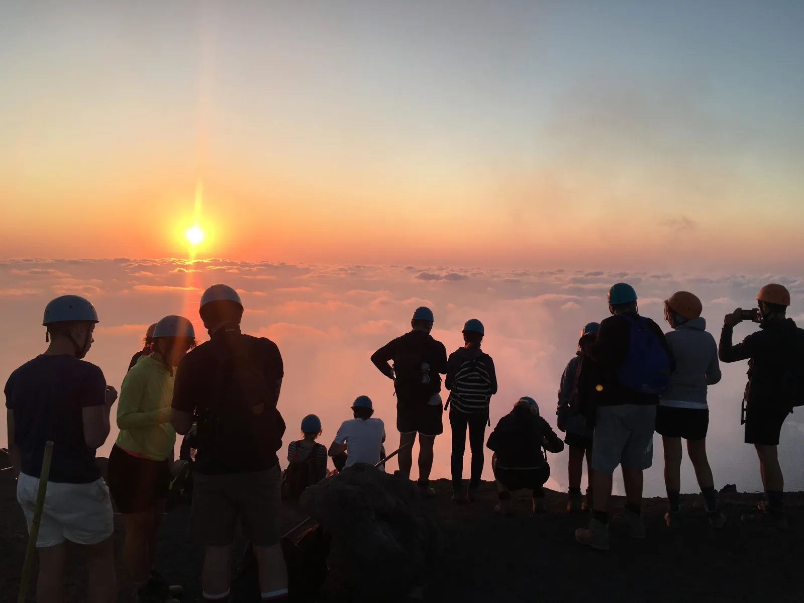 Hikers in silhouette watching the sunset from the volcano