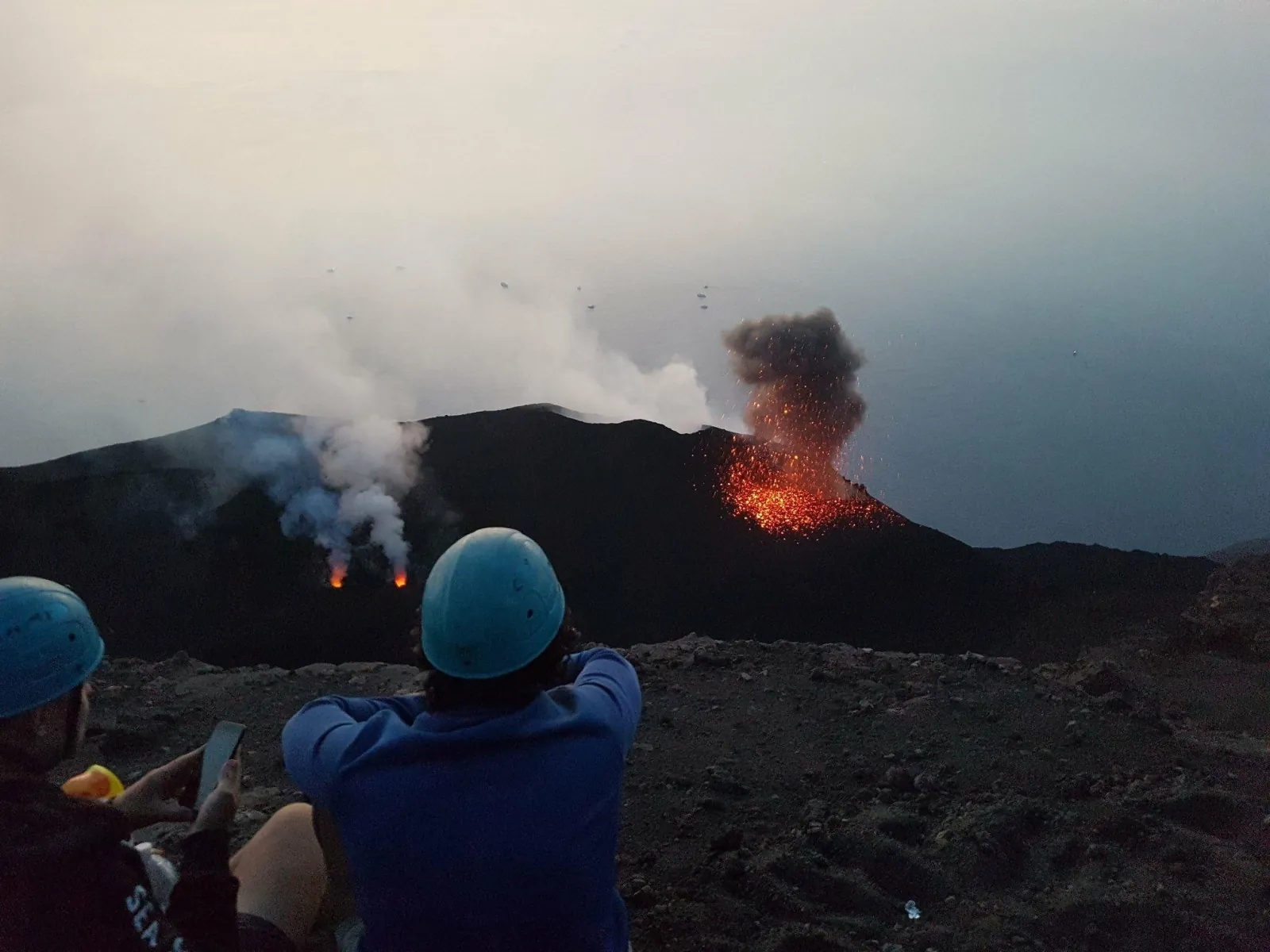 Hikers in helmets with a crater erupting below